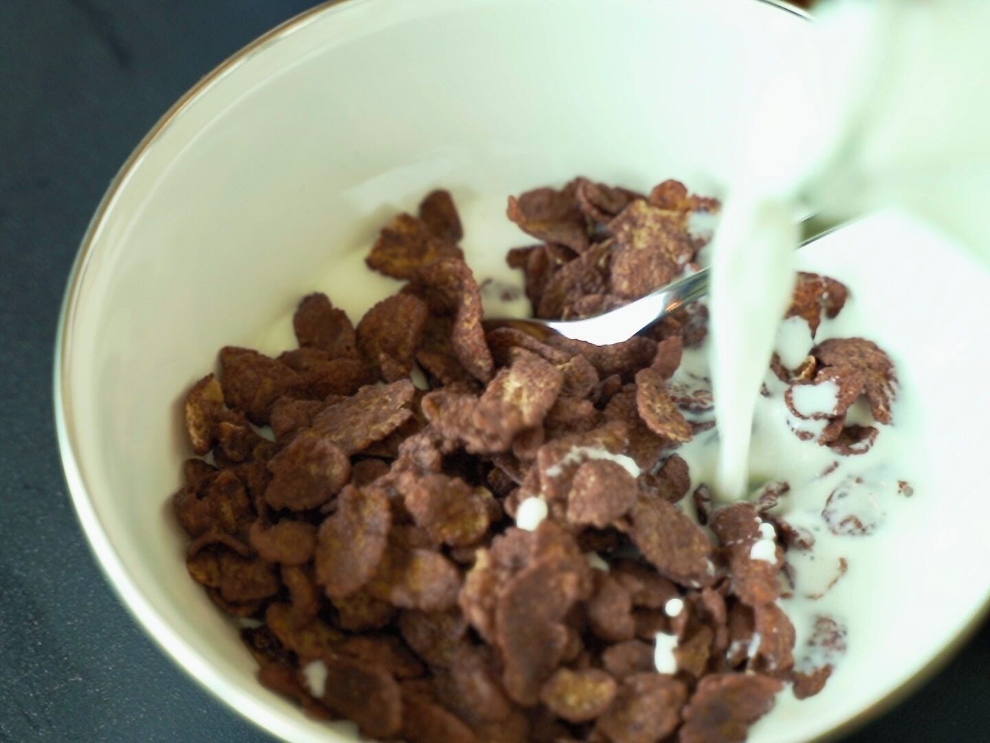 A bowl of cereal with milk being poured into it.