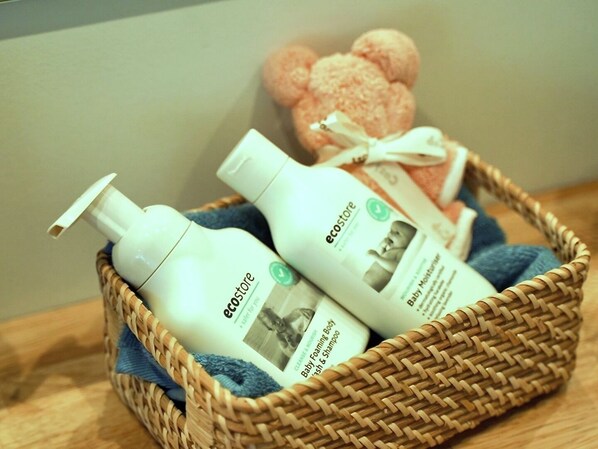 Un panier en osier contenant deux bouteilles de produits de soins pour bébés et une petite boîte cadeau.