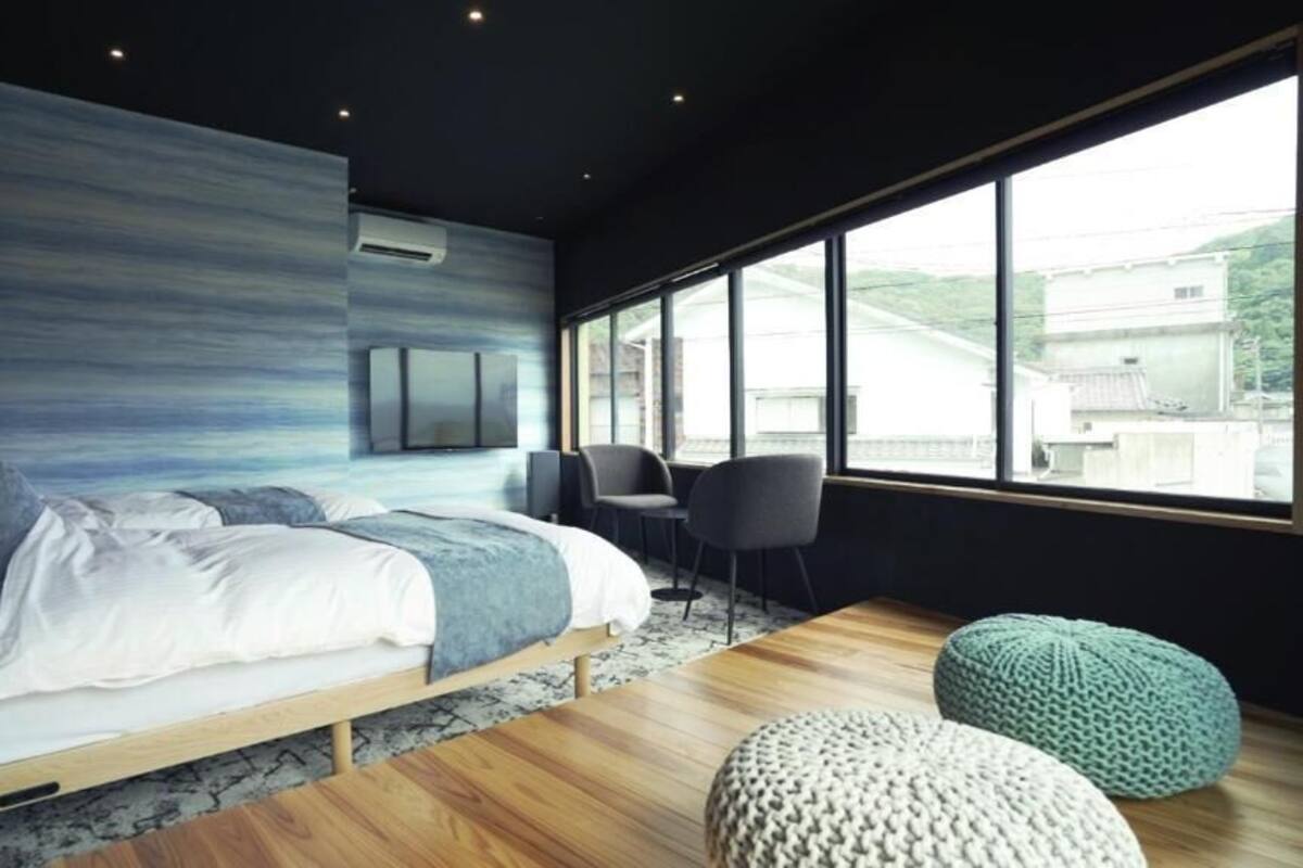 A modern bedroom with a bed, a seating area, and a large window.