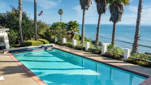 A swimming pool with a view of the ocean, surrounded by palm trees and a flag. - Beautiful Home above Mesa Bluffs (Santa Barbara)