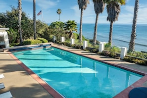 A swimming pool with a view of the ocean, surrounded by palm trees and a flag. - Beautiful Home above Mesa Bluffs (Santa Barbara)