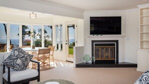 A living room with a fireplace, a television, and a view of the ocean. - Beautiful Home above Mesa Bluffs (Santa Barbara)