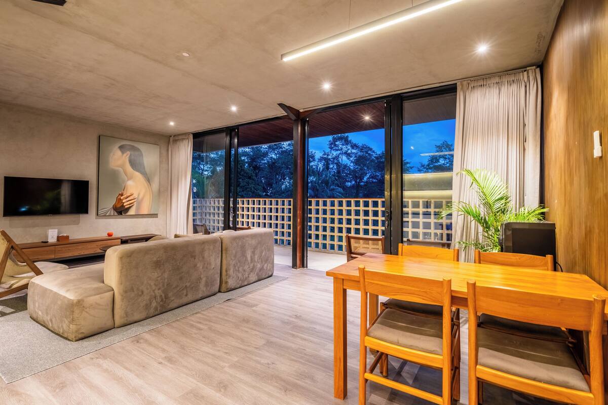 A modern living room with a sofa, a wooden dining table, and a TV.