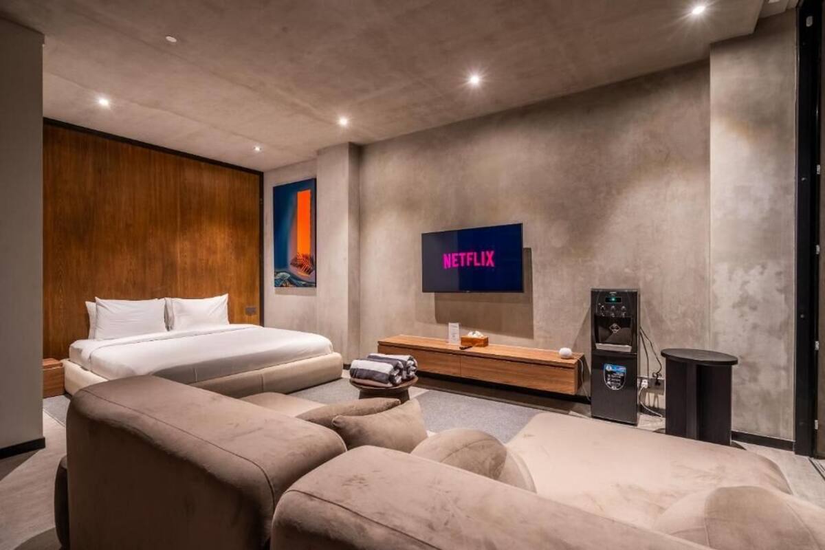A modern hotel room with a bed, a sofa, a TV, and a coffee machine.