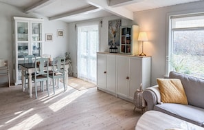 A cozy living room with a dining area, wooden floors, a sofa with a throw pillow, and a bookshelf.