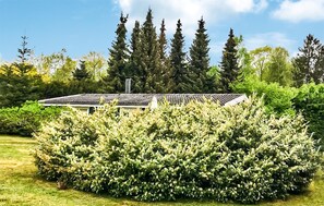 A building with a sloped roof, surrounded by dense shrubbery and tall trees.