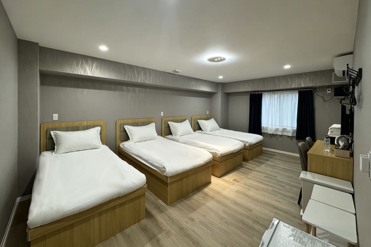 A hotel room with four single beds, a desk, a chair, and a small table.