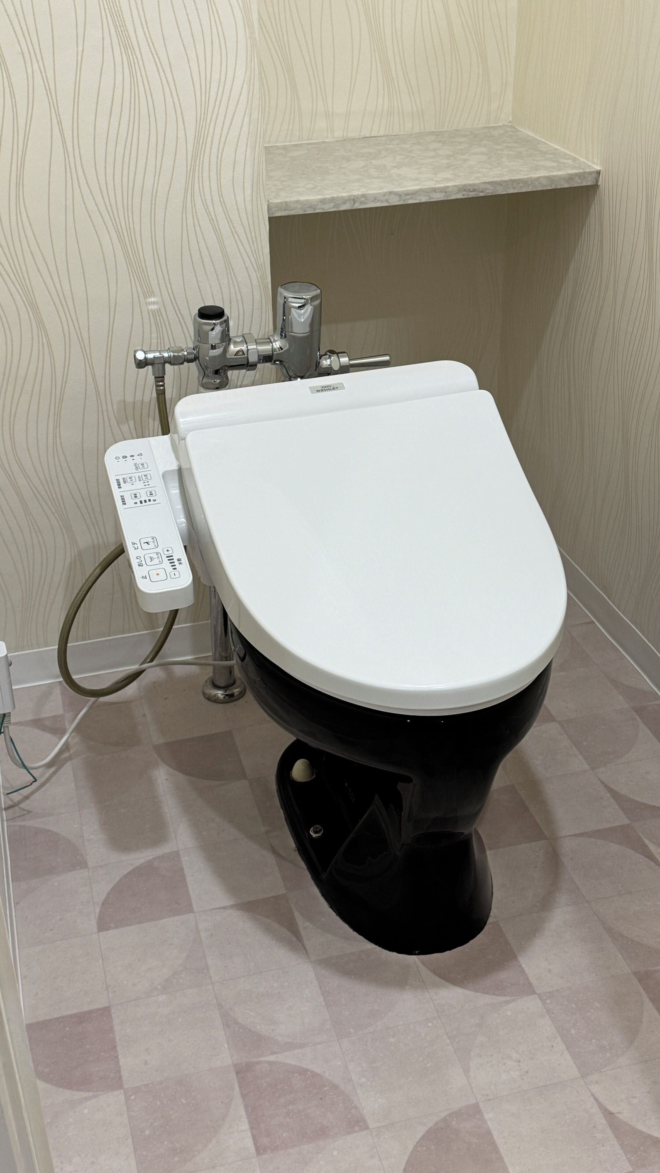A modern toilet with a control panel, a water tank, and a tiled floor.