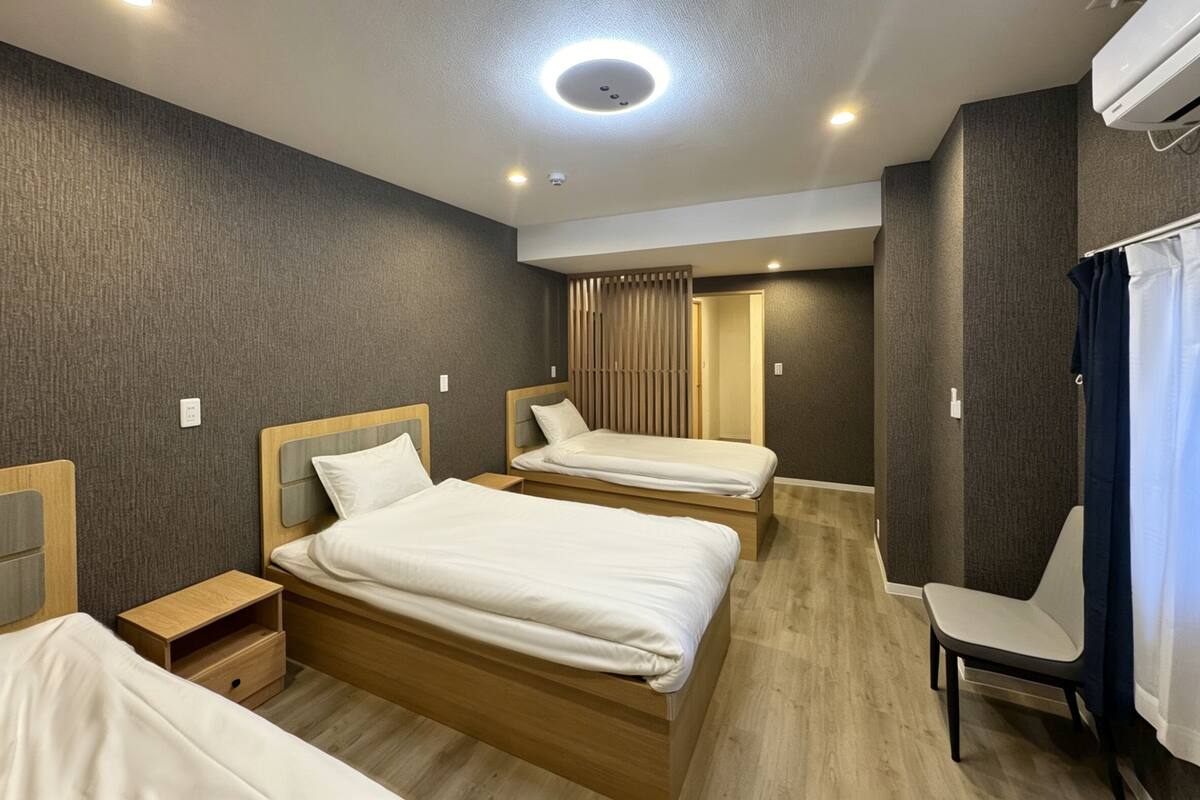 A hotel room with two beds, a chair, a desk, and an air conditioning unit.