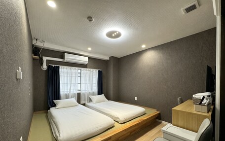 A hotel room with two beds, a desk, a chair, and a window with curtains.
