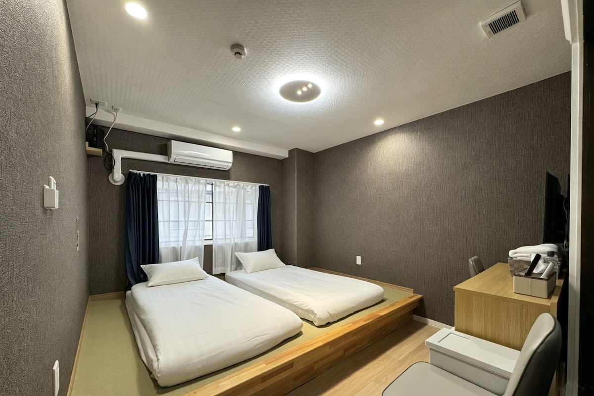 A hotel room with two beds, a desk, a chair, and a window with curtains.
