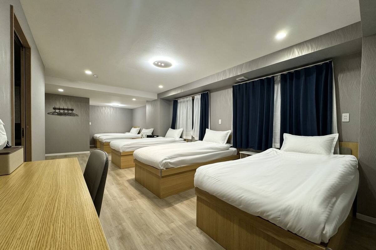 A hotel room with four single beds, a wooden desk, and a chair.