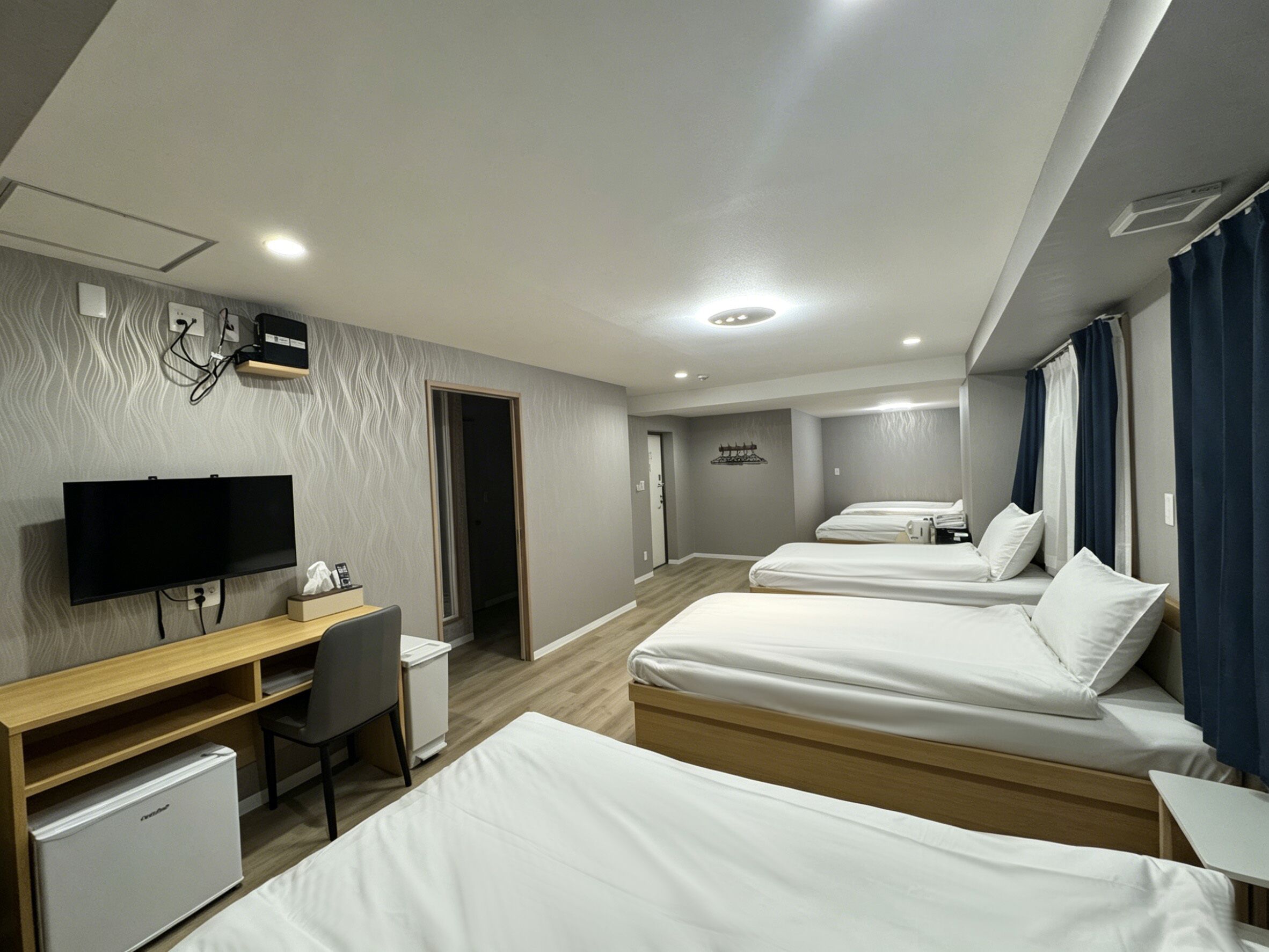 A hotel room with a TV, desk, chair, and three beds.