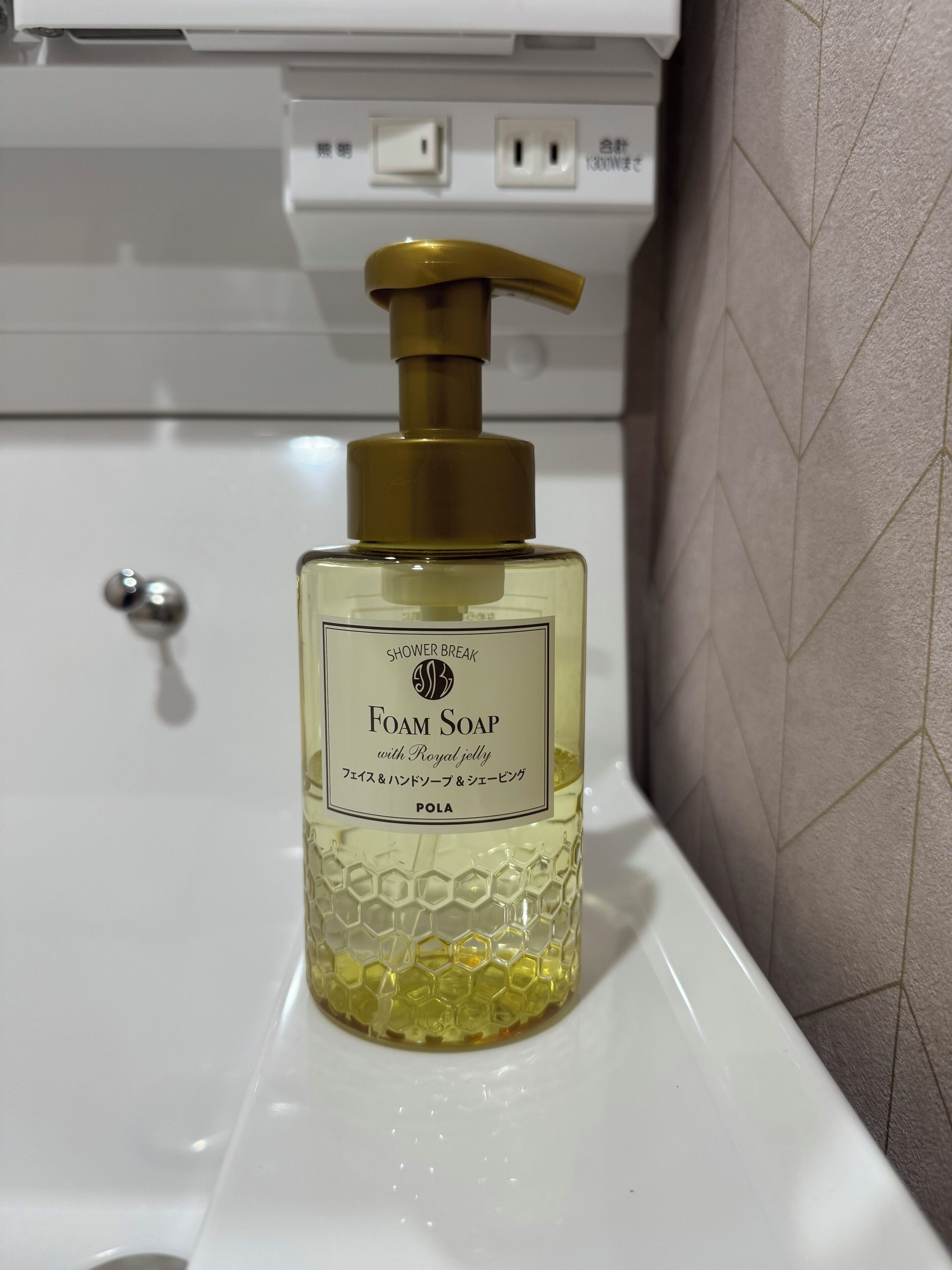 A bathroom with a white sink, a bottle of foam soap, and a wall with a geometric pattern.