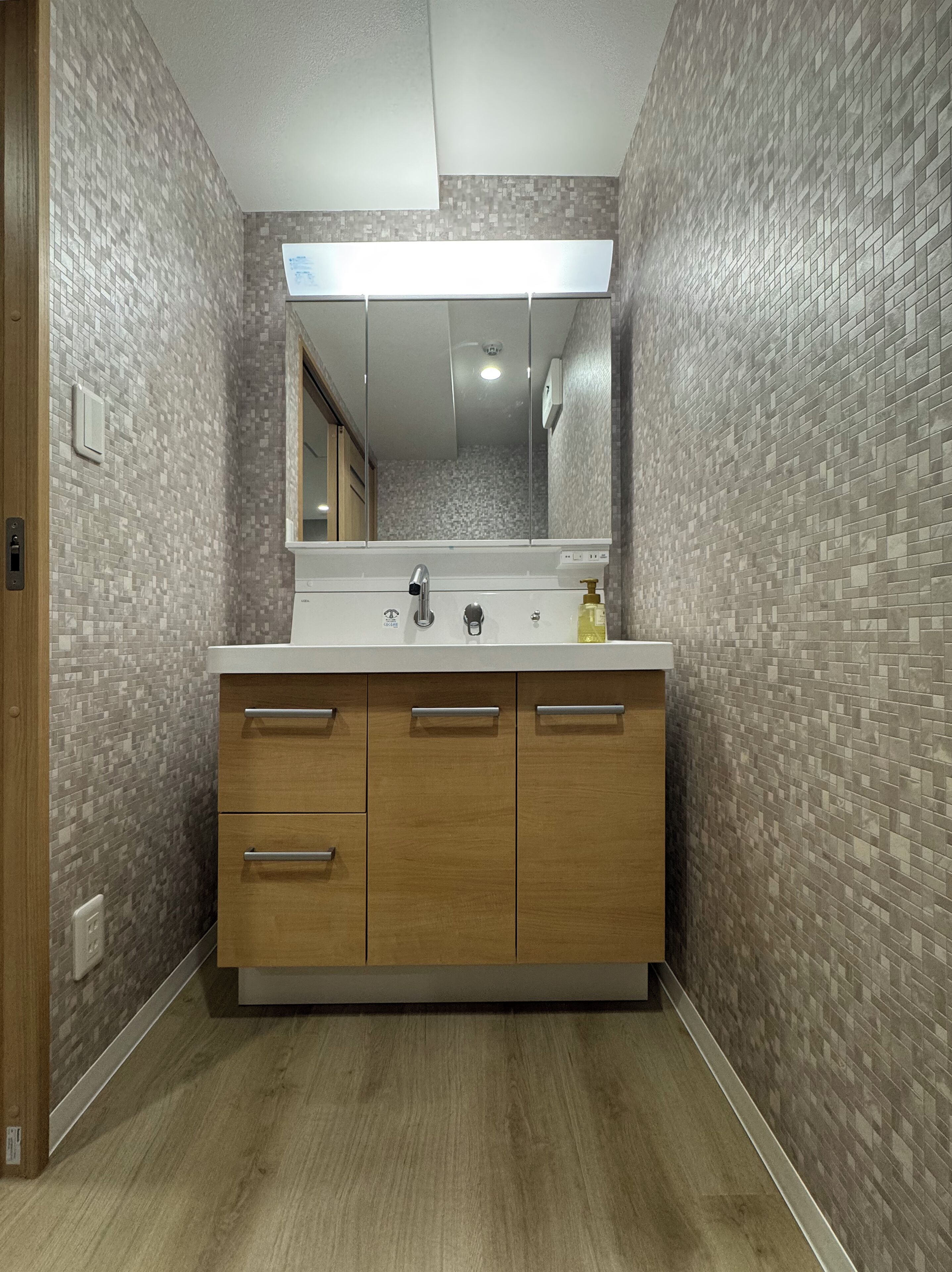 A bathroom with a tiled wall, a wooden vanity, a mirror, and a light fixture.