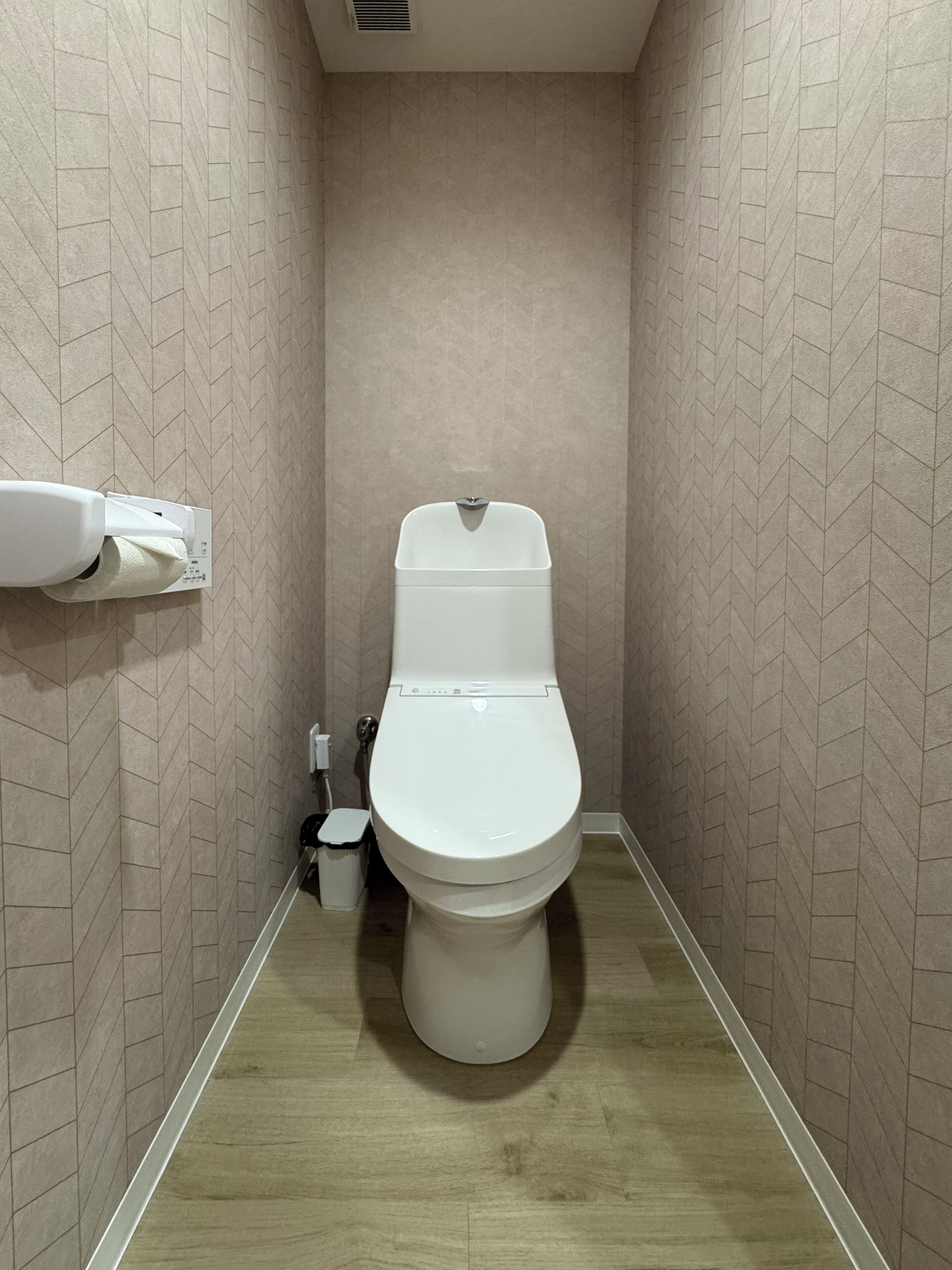 Un baño pequeño y estrecho con inodoro, secamanos y cubo de basura.