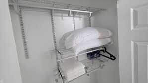 Ein weißer Schrank mit Metallregalen, einer Kleiderstange und einer Tür.