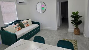 Ein modernes Wohnzimmer mit einem türkisfarbenen Sofa, einem runden Spiegel, einer Topfpflanze und einem Essbereich mit einem Marmortisch.