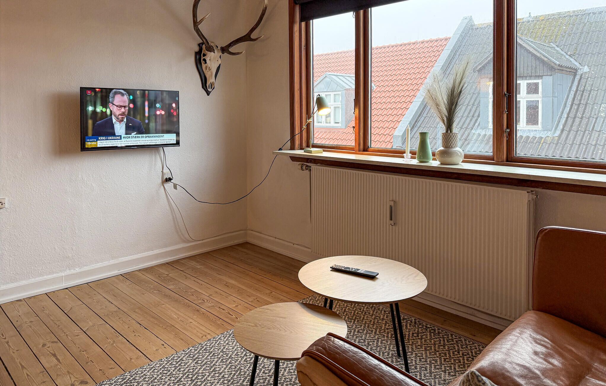 Huoneessa on seinälle asennettu televisio, ikkuna, josta on näkymä rakennuksiin, patteri, pieni pöytä ja nahkasohva.