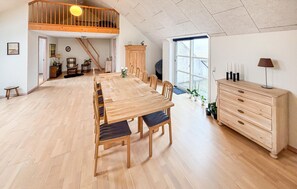 Ein geräumiger Essbereich mit einem langen Holztisch und Stühlen, einer Treppe, die in eine obere Ebene führt, und einem großen Fenster, das natürliches Licht hereinlässt.