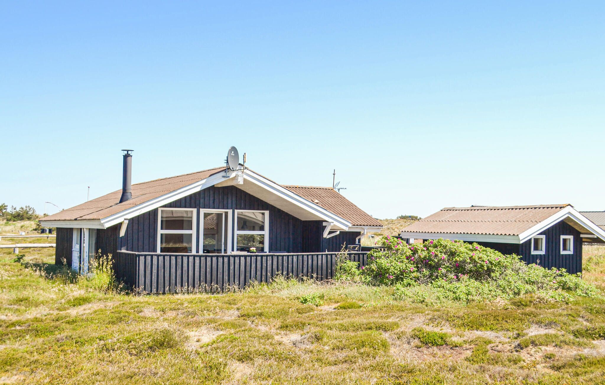 A small, single-story wooden house with a sloped roof, a chimney, and a satellite dish.