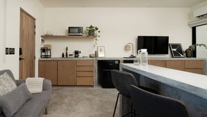 A modern kitchen with a built-in microwave, a coffee machine, and a small refrigerator. There is a wooden door and a grey sofa in the living area. - Loft 2 min walk from the Marina CSL (Cabo San Lucas)