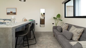 A modern living space with a kitchen area, a grey sofa, and a large window. - Loft 2 min walk from the Marina CSL (Cabo San Lucas)