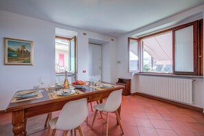 A dining area with a wooden table set for four, white chairs, a painting on the wall, and a window with a view.
