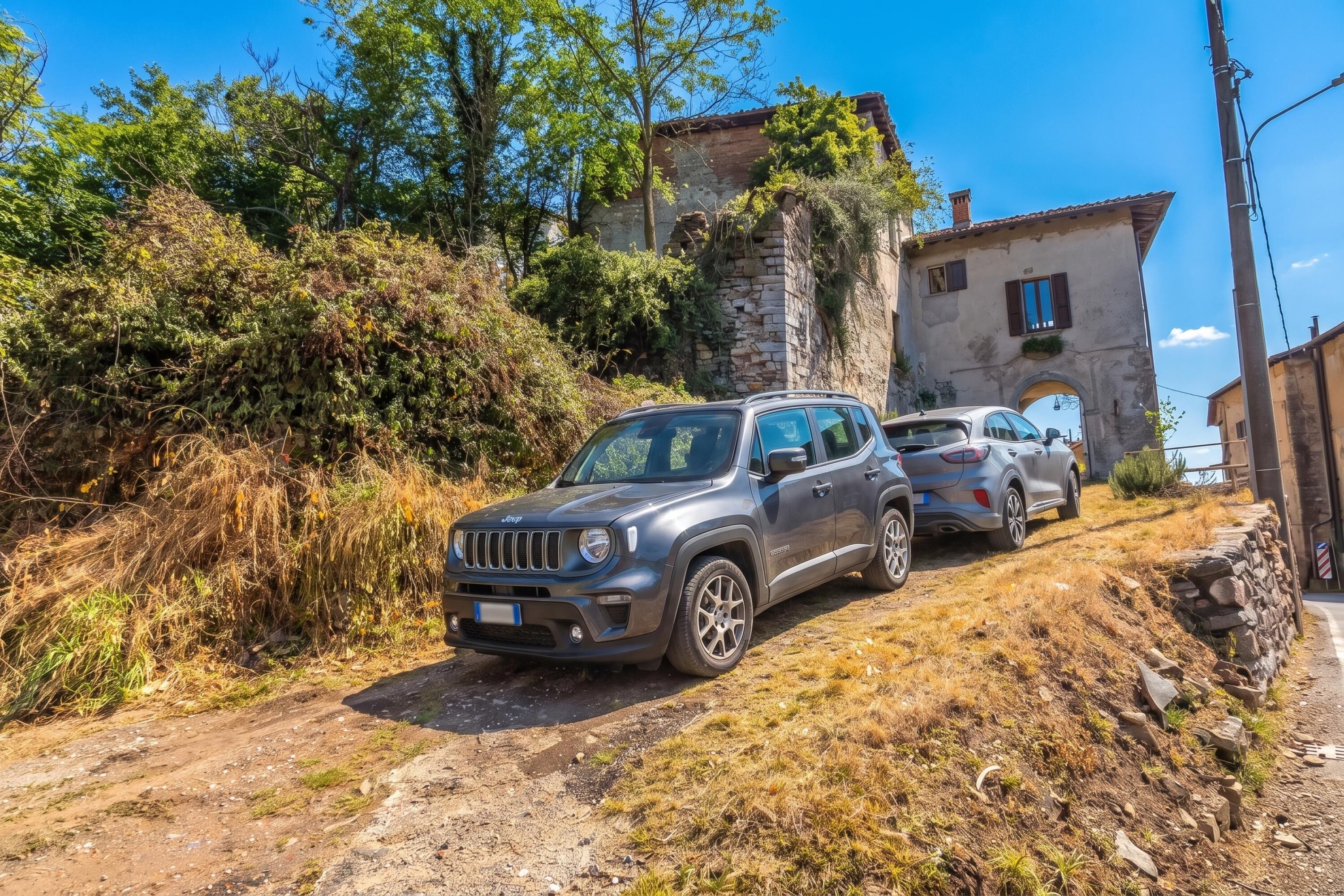 Un VUS Jeep est garé sur un chemin de terre, avec un bâtiment en pierre en arrière-plan.