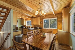 Interior de una cabaña de madera con comedor, cocina y una escalera.