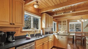 A modern kitchen with wooden cabinets, stainless steel appliances, and large windows offering views of the outdoors.