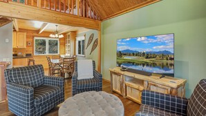 A cozy cabin interior with a wooden ceiling, a dining area, and a TV displaying a scenic landscape.
