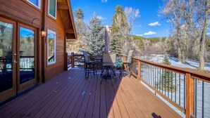A wooden deck with outdoor furniture and a covered grill area, overlooking a snowy landscape with trees.