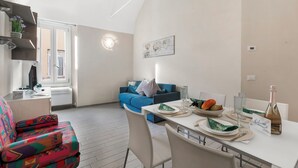 A modern living room with a sofa, a dining table set with plates, glasses, and a bottle, and a blue couch in the background. - Garibaldi - Loano Centre Apartment for 4, Loano, Italy (Loano)