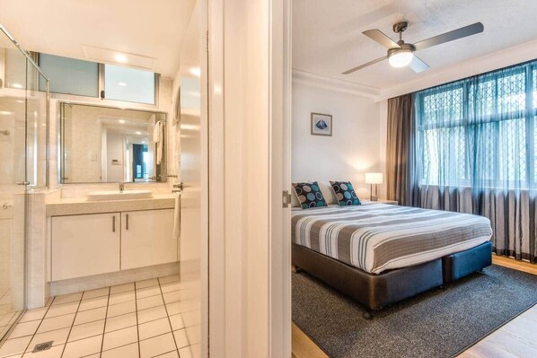 A bedroom with a bed, a nightstand, a lamp, a ceiling fan, and a window with curtains. - Frangipani Lodge 101 (Hamilton Island)