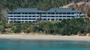 A multi-story hotel with a flat roof, located near a beach with clear blue water. - Frangipani Lodge 101 (Hamilton Island)