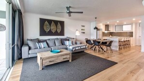 A modern living room with a sofa, coffee table, and dining area. - Frangipani Lodge 101 (Hamilton Island)