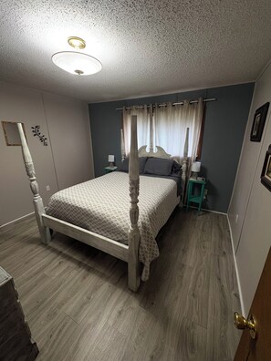 A four-poster bed with a canopy, a nightstand, a lamp, and a mirror on the wall.