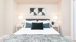 Ein Schlafzimmer mit einem Bett, zwei Nachttischen, einer Wandlampe und einem gerahmten Bild.