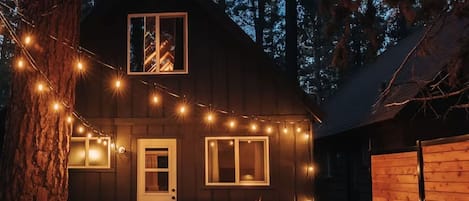 A cabin with a deck, a fire pit, and string lights.