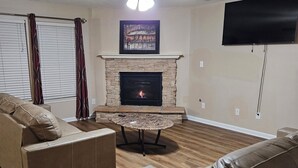 Una sala de estar con chimenea, dos sofás, un ventilador de techo y un televisor de pantalla plana.