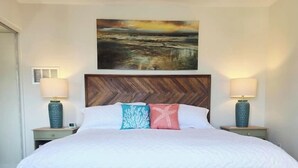 Een slaapkamer met een groot bed, twee nachtkastjes, een bankje en een schilderij boven het bed.