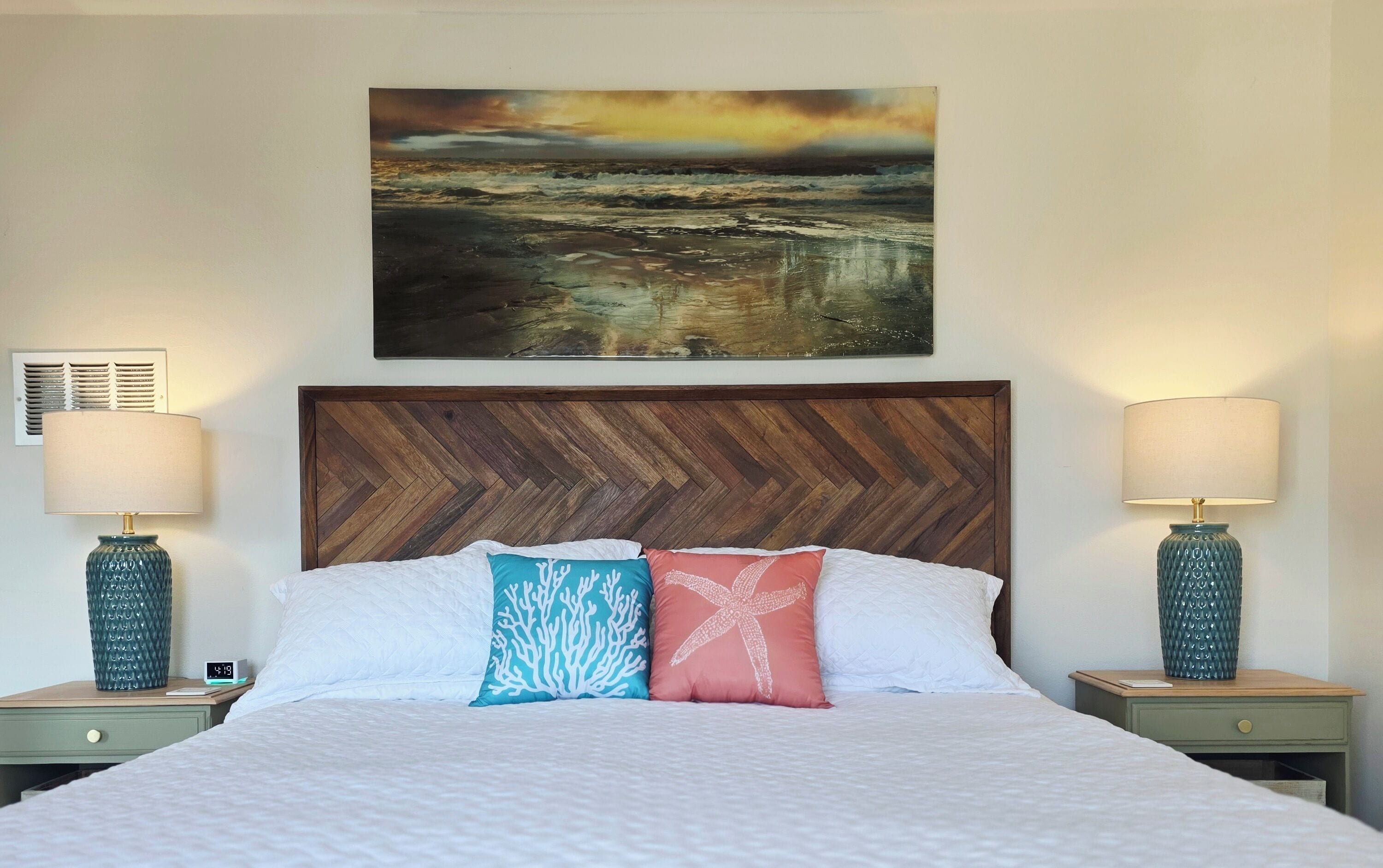 A bedroom with a wooden headboard, a bed with white bedding, two nightstands with lamps, and a painting above the bed.