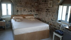Un dormitorio con pared de piedra, estructura de cama de madera, una mesita de noche y una ventana.