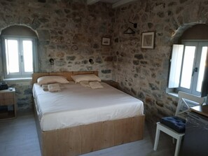 A bedroom with a stone wall, a wooden bed frame, a bedside table, and a window.
