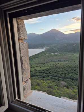 A view from a window overlooking a valley with mountains, a lake, and scattered buildings.