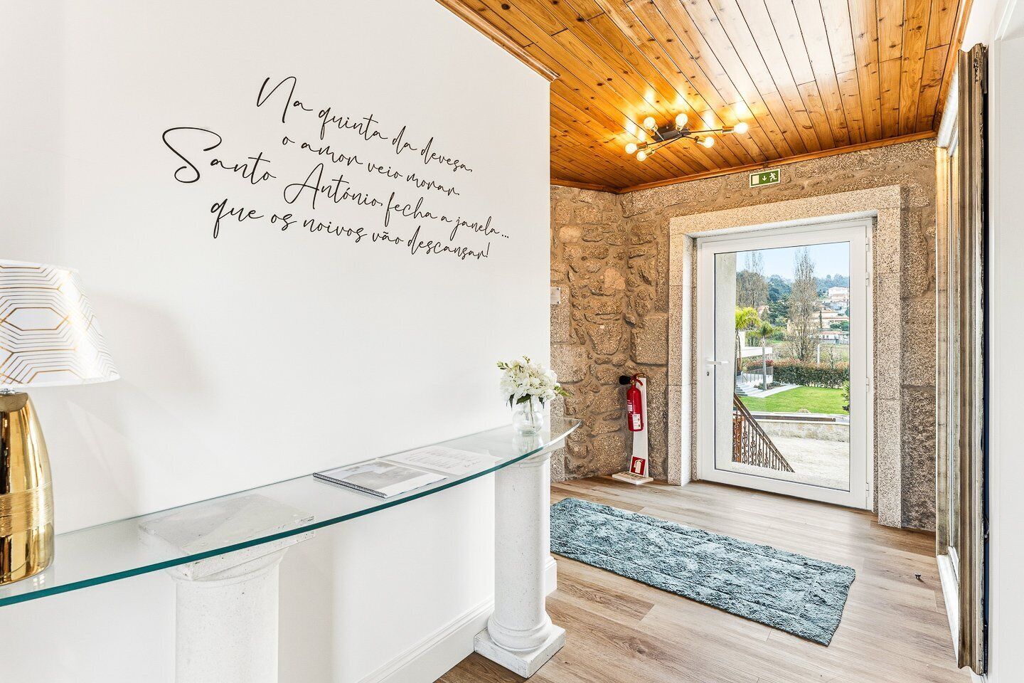 Un espace d’accueil avec un comptoir en verre, un panneau fixé au mur, un extincteur et une vue à travers une porte vitrée.