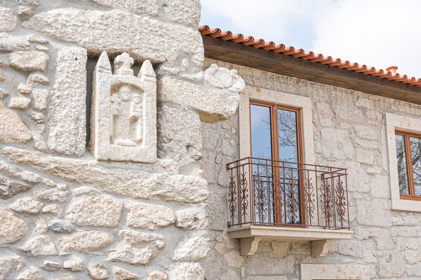 Edifici de pedra amb un balcó que té barana de ferro forjat i una finestra amb talla de pedra decorativa.