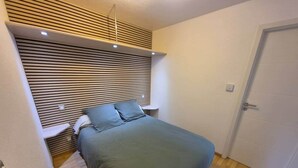 Quarto com uma cama, mesa de cabeceira, luminária na parede e uma porta.