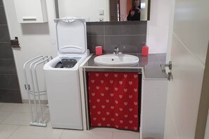 A compact bathroom with a washing machine, a sink, and a red heart-patterned shower curtain. - Downtown Colmar, parking lot, terrace, air-conditioned, private parking (Colmar)